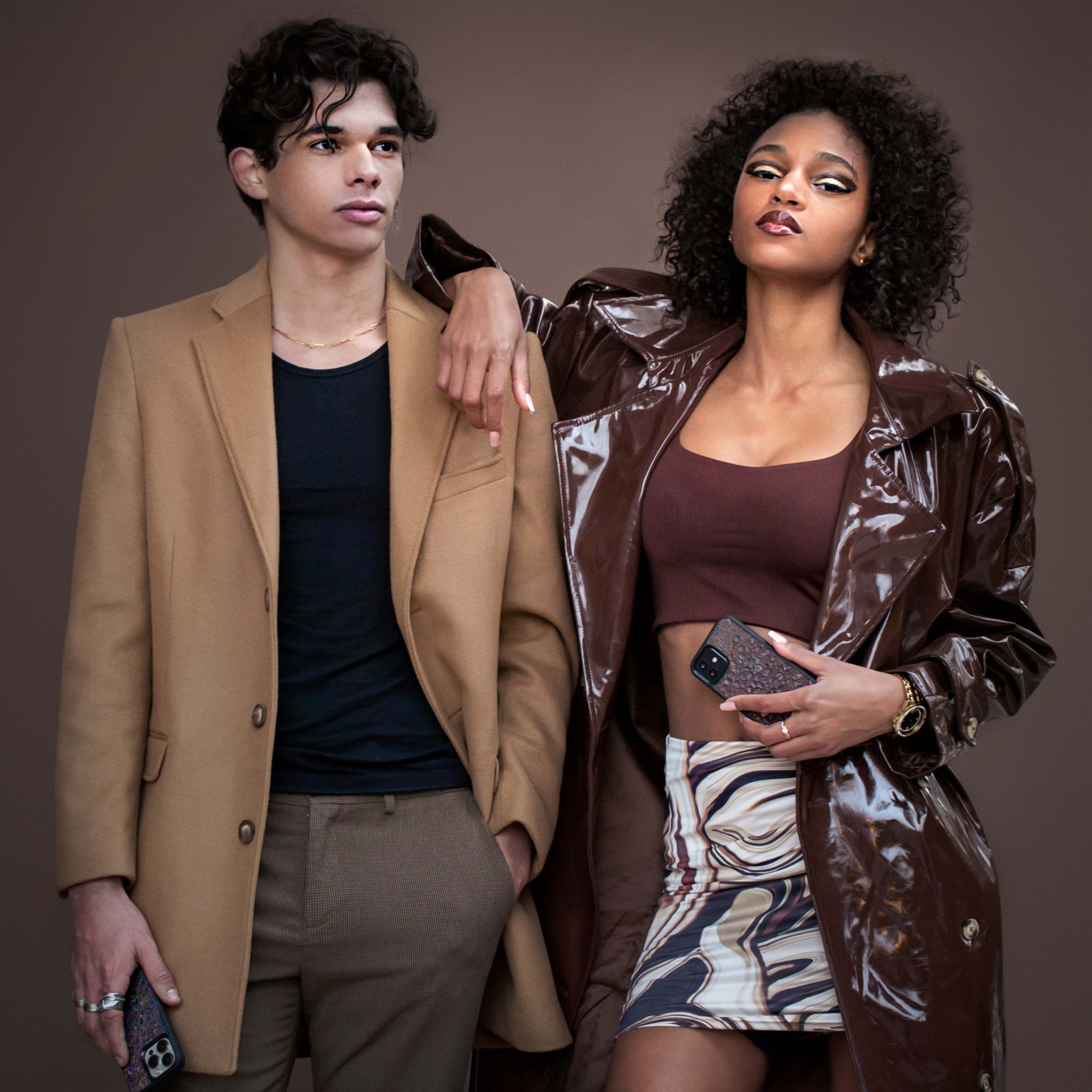 Un homme et une femme portant tous les 2 vêtements de thème marron prennent la pose. Ils ont également tous les 2 une coque Hibisca en café Arabica. Leurs coques sont de couleur marron. 